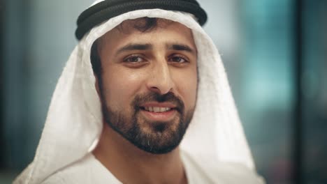 portrait of successful arab businessman in traditional outfit gently smiling, wearing white kandura and black agal keeping a ghutra in place. saudi, emirati, arab businessman concept.