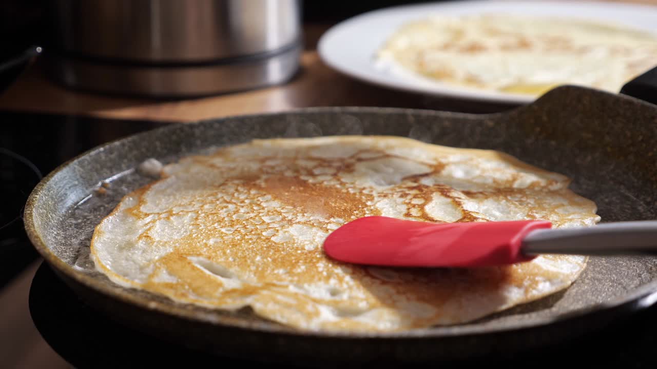 Unrecognizable woman turns a pancake in a frying pan with a spatula close-up