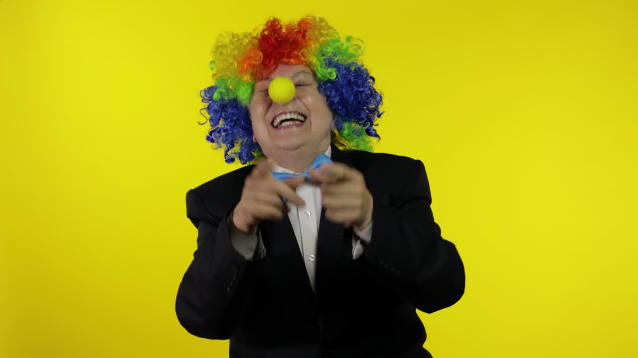 anciana payasa en peluca colorida sonriendo, tonto alrededor, riendo. halloween