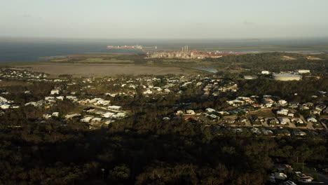 sobrevuelo aéreo pueblo rural con árboles y planta de energía industrial y el océano pacífico en segundo plano.