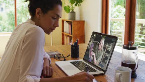 Mixed-race-businesswoman-sitting-at-desk-using-laptop-having-video-call-with-female-colleague