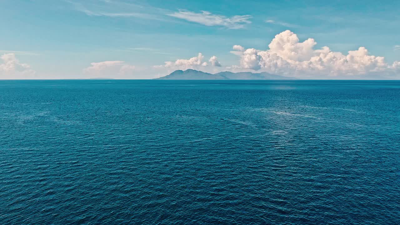 Aerial drone ascending above the water's surface, a scenic oceanscape horizon unfolds, featuring a distant island on the horizon, Philippines
