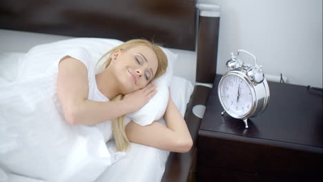 pretty sleeping woman with alarm clock next to her