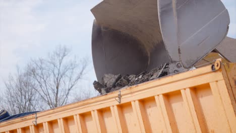 a heavy bulldozer loads rubble onto the loading truck on a low angle view.