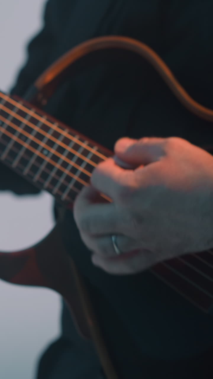un guitarrista sin rostro está tocando una guitarra contra un fondo blanco, con otra guitarra visible en el fondo. el primer plano se centra en las manos del músico y la guitarra