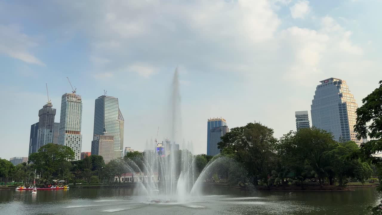 Lumpini park Bangkok Thailand green space water pond sprinkle, city buildings skyline