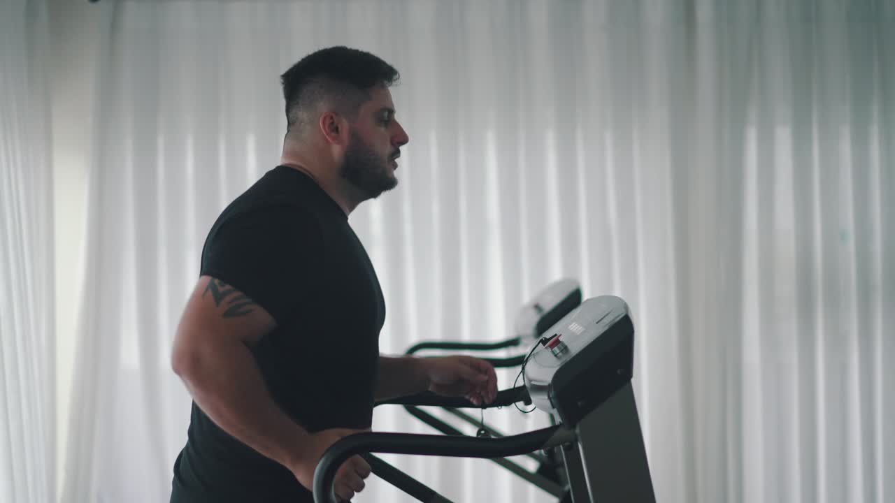 Uomo forte che si allena con esercizi cardio sul tapis roulant in palestra, vista laterale.