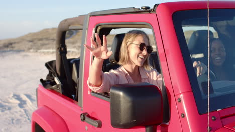 young caucasian woman and african american woman enjoy a sunny day in a pink jeep on a road trip, wi