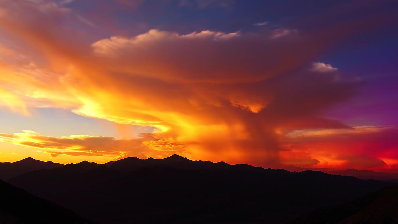 Vibrant sunset over mountain silhouette with dramatic orange clouds