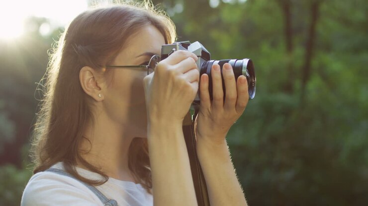 Side view of a beautiful young woman in glasses taking photos in the park with a old vintage photo camera