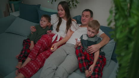 Family-of-three---father-mother-and-tow-son-watching-TV-in-the-evening.-Togetherness-quarantine-stay-home.-High-quality-4k-footage