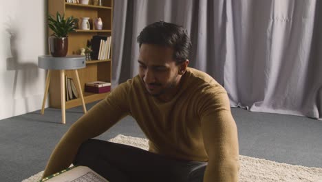 muslim man at home sitting on floor and reciting from the quran 1