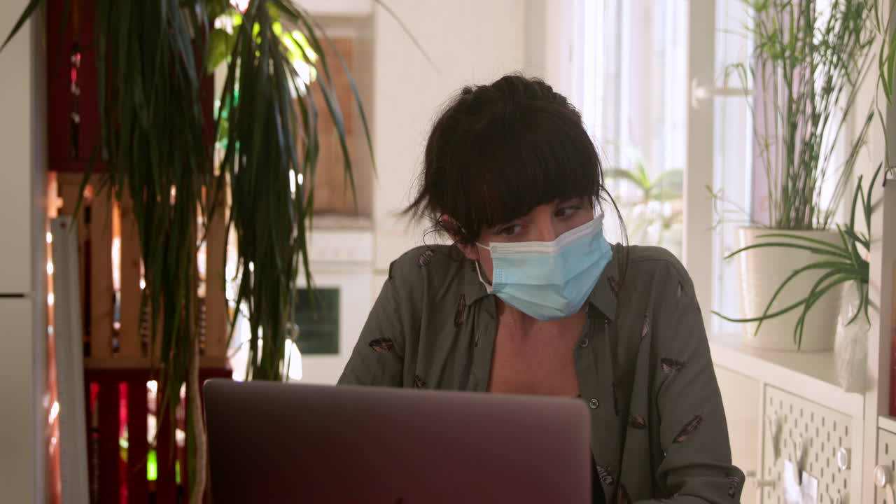 Brunette woman video calling through computer with mask at home