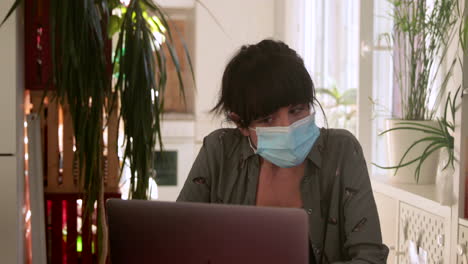 brunette woman video calling through computer with mask at home