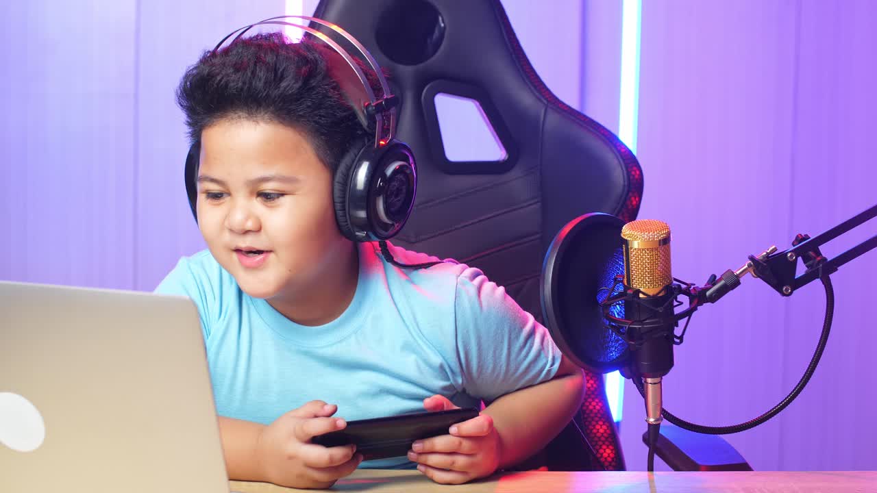 Asian Little Boy Holding Mobile Phone And Read Comment In Laptop Computer Then Talking To Camera While Live Stream