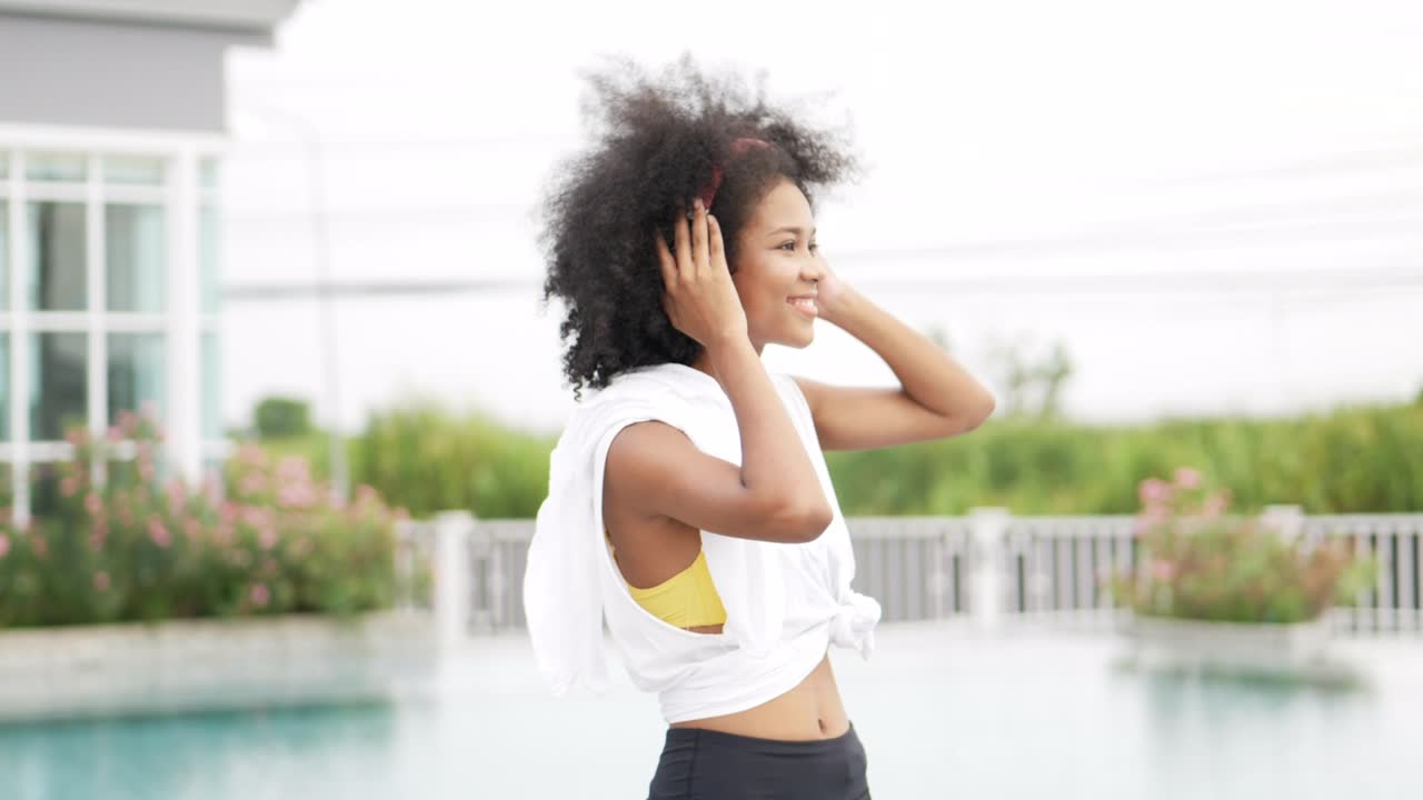 mujer africana en ropa deportiva con auriculares bailando en el fondo de la piscina