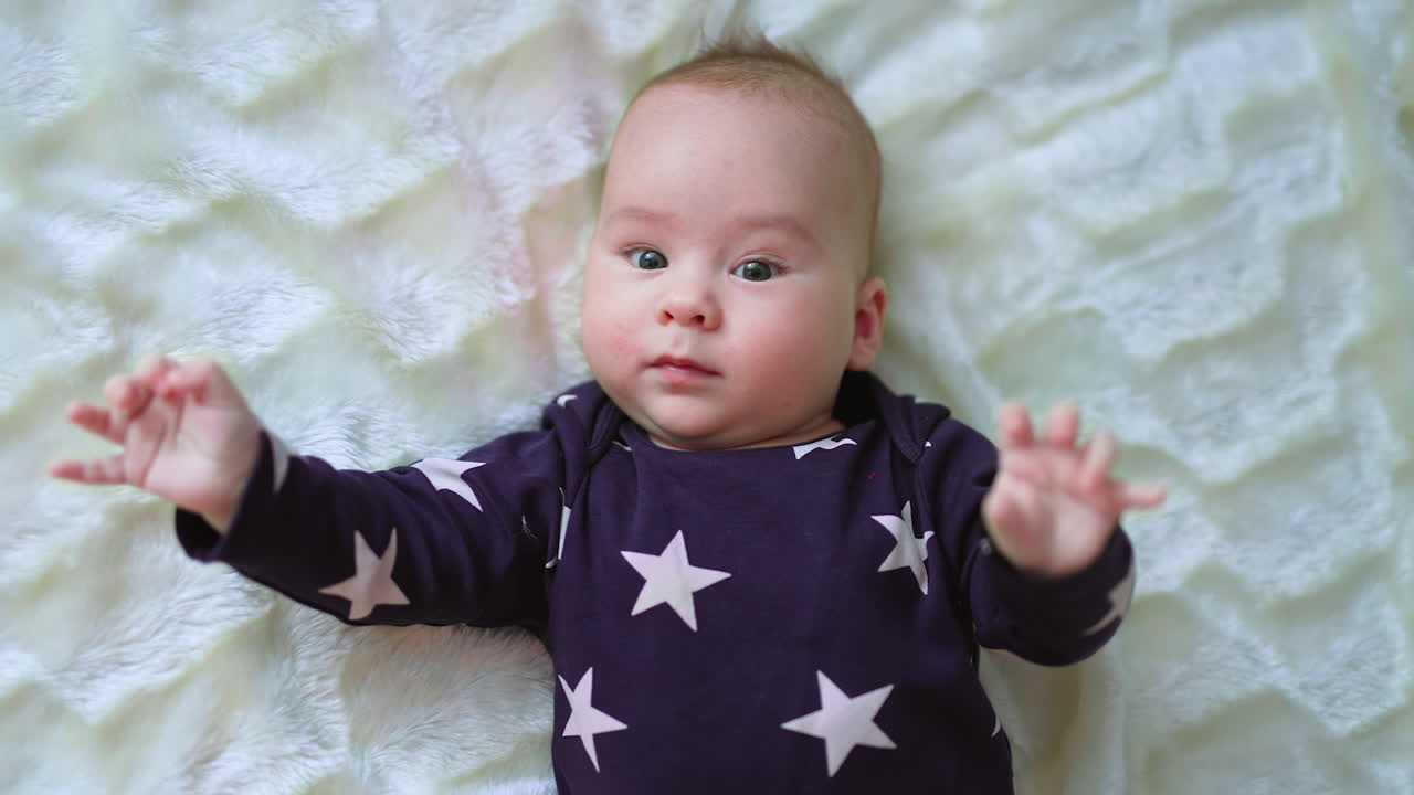 Happy cheerful healthy kid on the bed. Baby boy in dark sweater with stars on white backdrop. Close up. View from top.