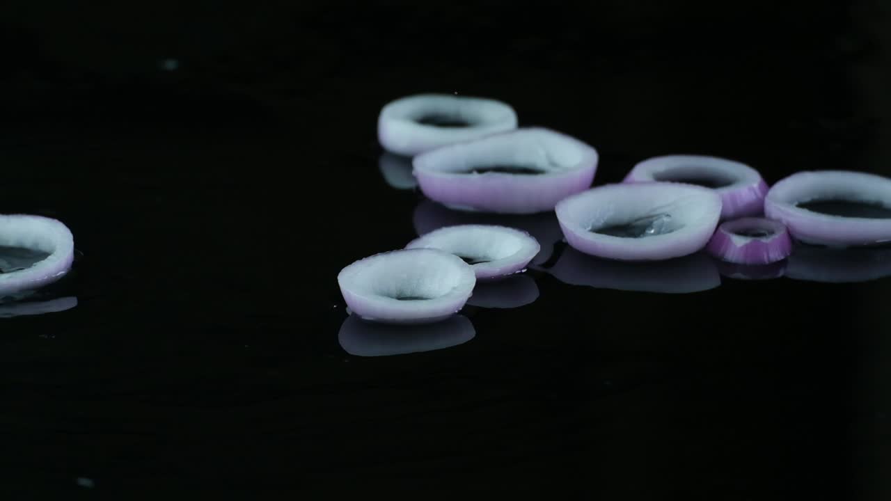 anillos de cebolla roja en rodajas sobre un fondo negro mojado, toma de estudio