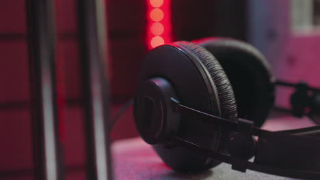 close-up of black over-ear headphones in a dimly lit studio room, illuminated by dynamic green, blue, and red lighting. t mood of a professional audio setup with subtle light reflections