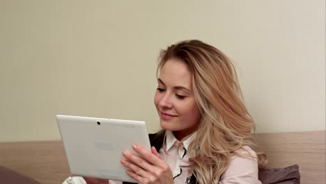 una joven agradable y sonriente usa una tableta digital haciendo compras en línea sentada en una cama en casa