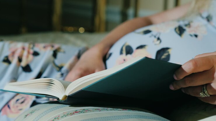 la donna incinta legge un libro nel suo colpo del primo piano del letto