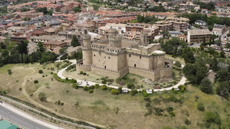 epic cinematic aerial of the new castle of manzanares el real showing the historic landmark at the foot of the sierra de guadarrama and the surrounding town in the community of madrid spain