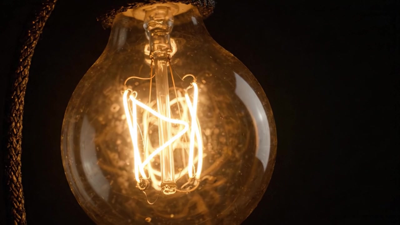 Vista Ravvicinata di una Lampadina Edison Vintage che si Illumina con un Design Unico del Filamento su Sfondo Scuro.