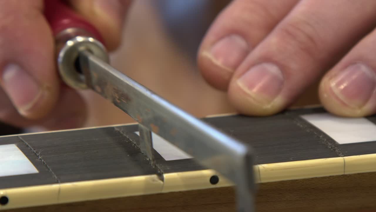 Sega per tasti che taglia una fessura sulla tastiera in ebano di una chitarra elettrica in negozio.