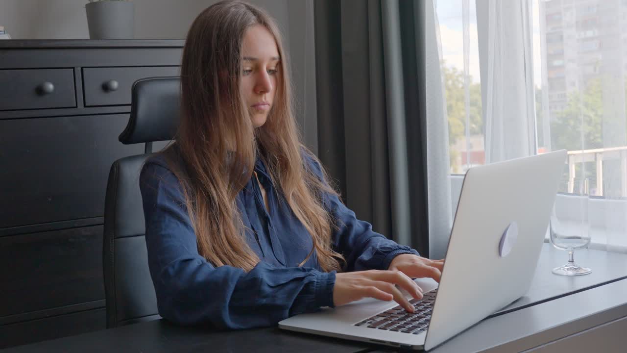 Young white woman sitting at her desk typing on laptop, home office, focus