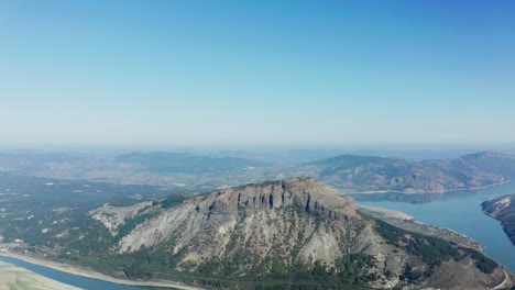 Aerial-view-of-a-mountain-top,-surrounded-by-a-river-and-a-big-blue-sky