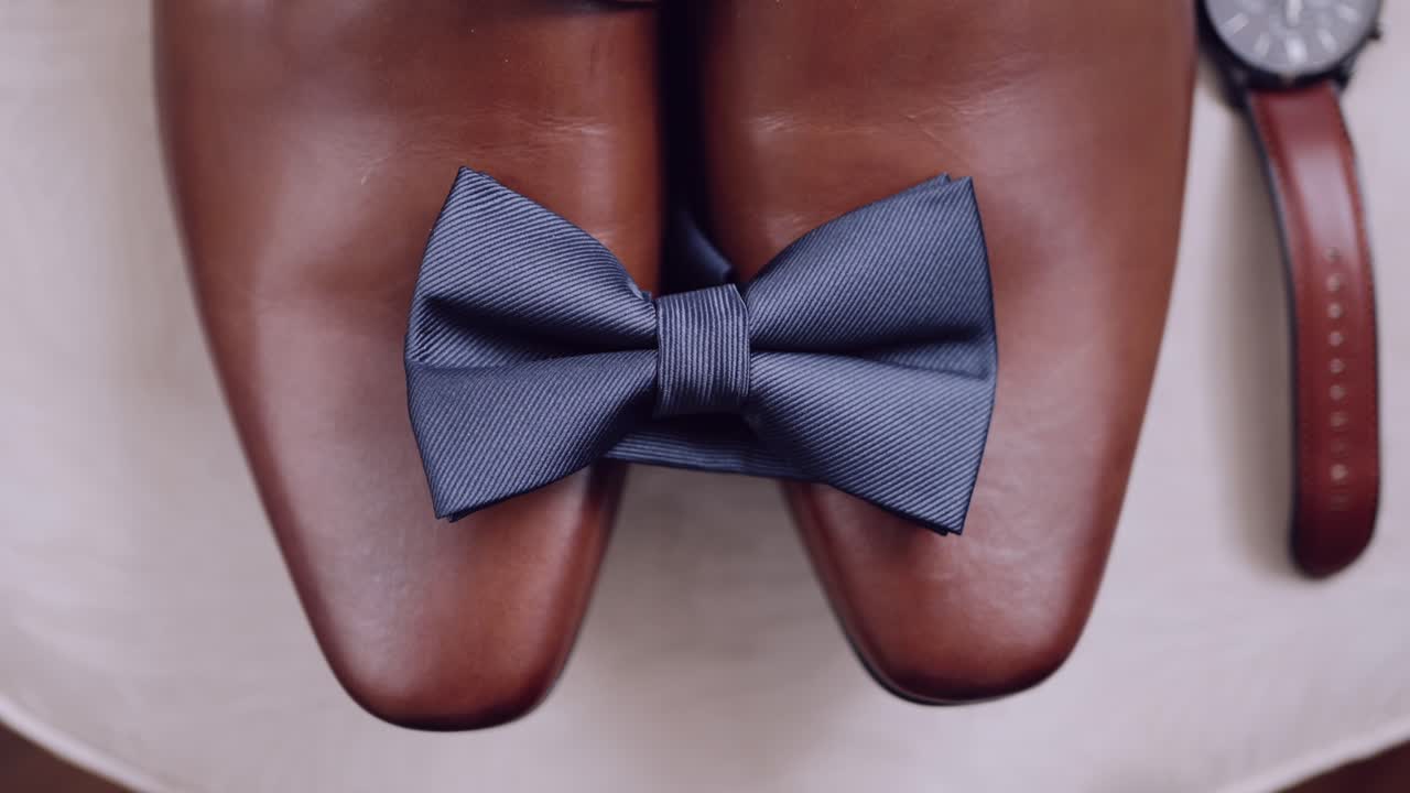 Close up of polished brown leather shoes with a blue bow tie elegantly placed between them