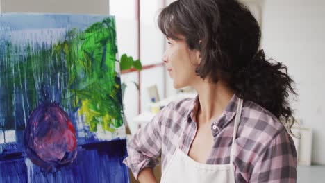 video of happy biracial female artist posing with painting in studio