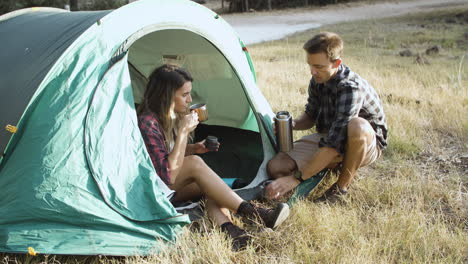 un par de excursionistas bebiendo café de un termo en el camping