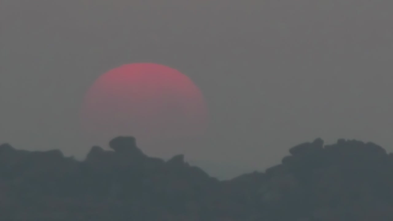 Timelapse, a large sun sets in orange clouds that turn blue