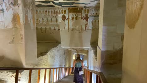 young woman with a hat descending the stairs of a sacred tomb that leads to a sarcophagus decorated with paintings in the valley of the kings