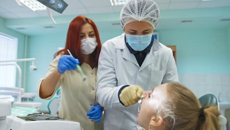 female student of dentistry department inserts metal instrument into patient's mouth. teacher is guiding and helping the student.