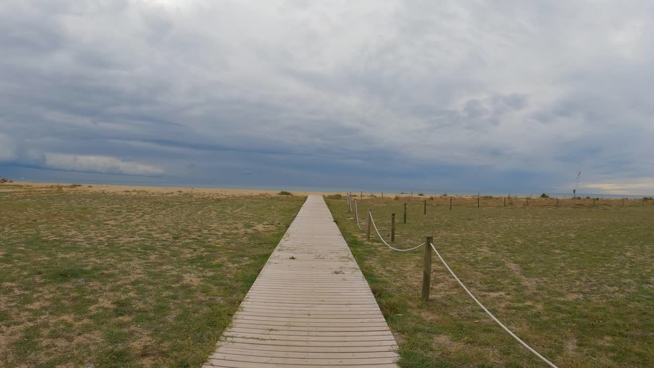 Wooden bridge over the sand direction to the beach walking in slow motion gimbal drone cloudy stormy day