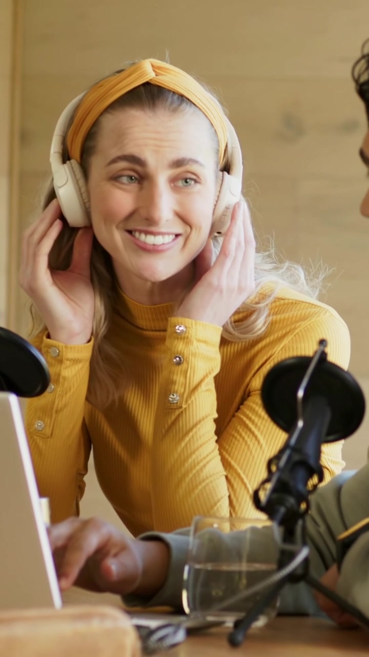 Vertikal video: Tager headset på, vært i gul top justerer sig i studie for at optage, med mikrofoner.