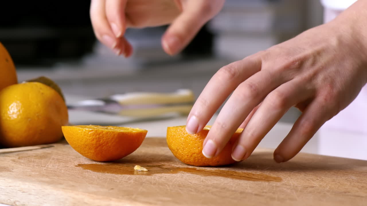 Woman slicing orange in two parts on a wooden board. Fruits on the background. Slow motion
