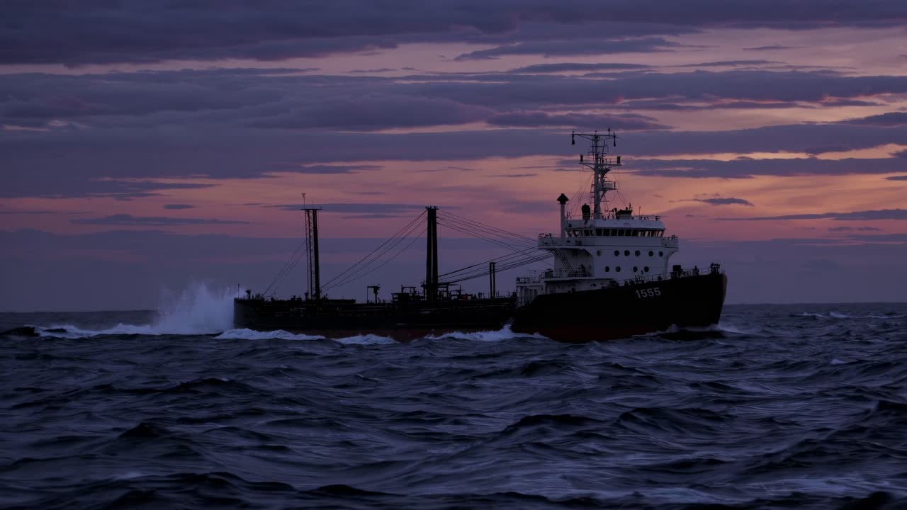A dramatic wide-angle shot of a cargo ship sailing at dusk, capturing the moody ocean waves and sky