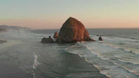 low circling aerial shot over haystack rock at sunset