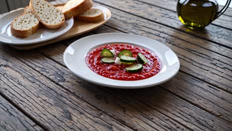 chilled gazpacho. a traditional spanish cold tomato soup. presented with fresh sliced cucumber. creamy cheese. and crusty bread. all arranged on a rustic wooden table with olive oil in a glass cruet