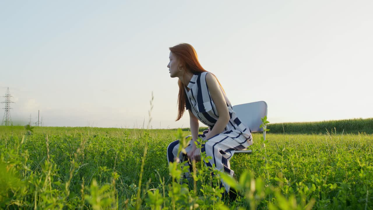 해가 지는 동안 들판에 앉아 있는 줄무 옷을 입은 여자