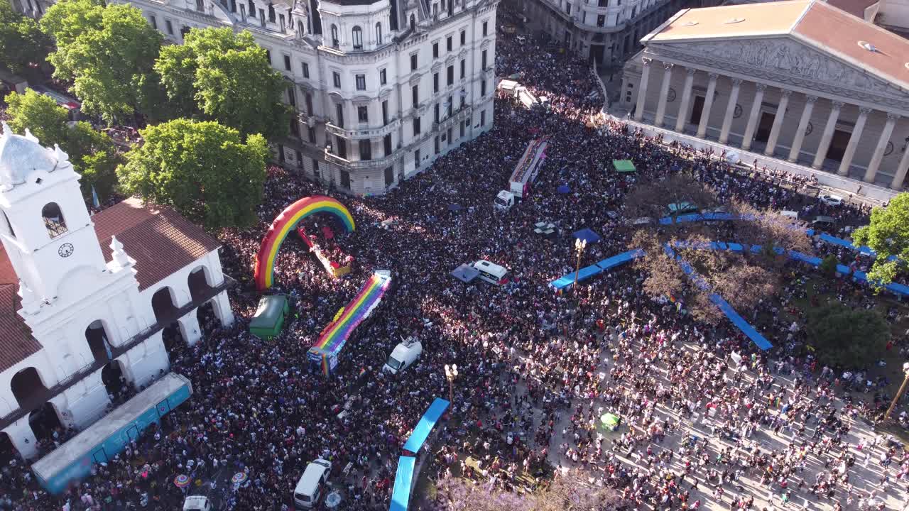 toma en órbita aérea del desfile del orgullo lgbt en buenos aires en plaza de mayo con banderas coloridas a la luz del sol
