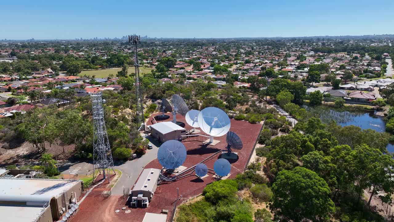 Satellite Facility With Communication Dishes And Towers Surrounded By Suburban Homes, Greenery, And Lake. wide aerial shot