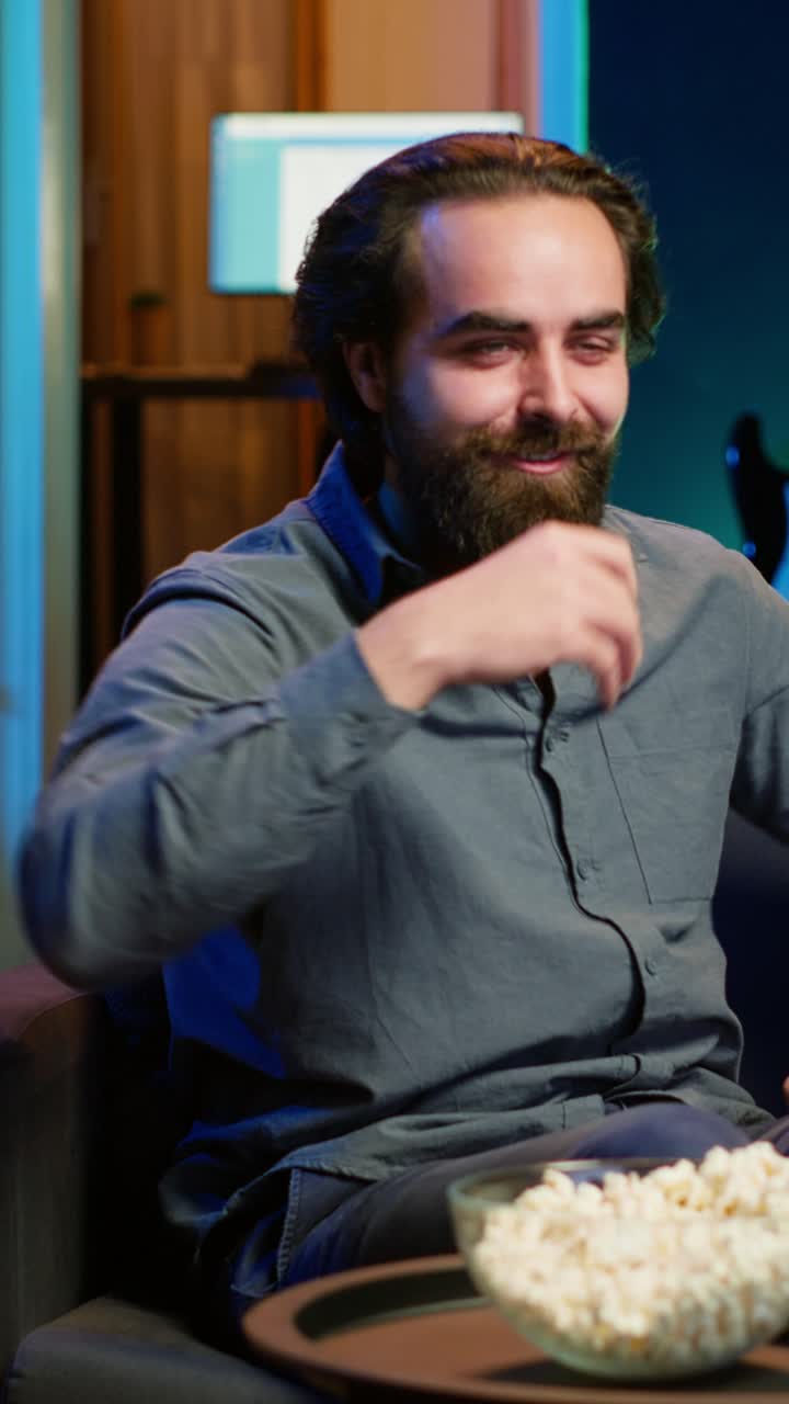 Vertical video Overjoyed man sitting on couch laughing while watching funny comedy movie