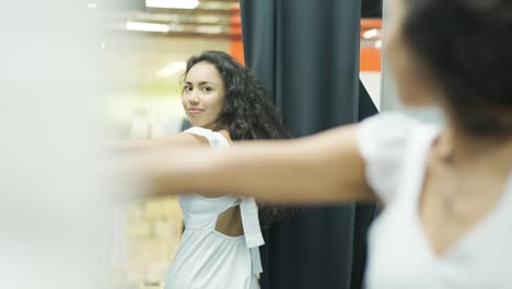 happy, stylish girl trying on outfit in dressing room in interior boutique clothing store with bright lighting.