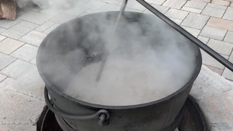 mixing ground meat or puttens in an iron kettle over a wood fire