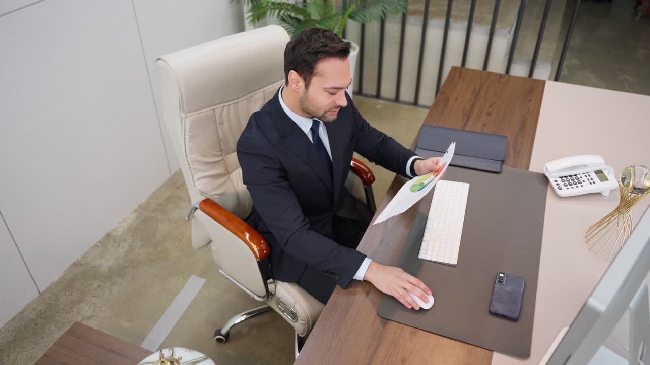 High angle view of a busy thoughtful European businessman analyzing financial sheet documents checking data on computer while sitting at workplace in a business office.
