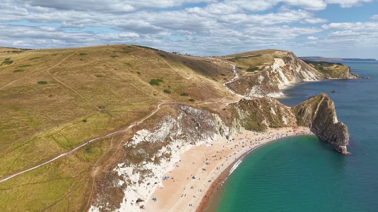 Filmato con drone che vola verso la spiaggia affollata e l'iconico arco di Durdle Door, Dorset